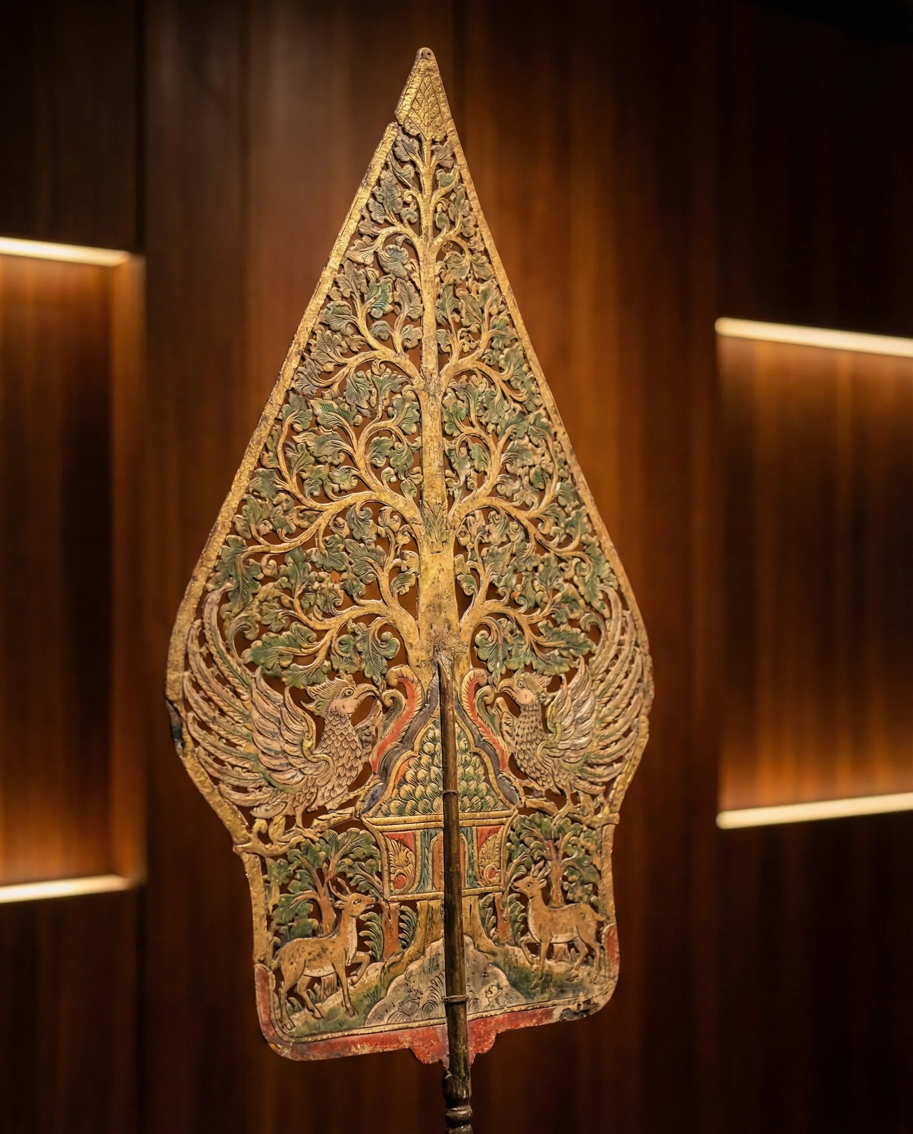 Detail ukiran gunungan: motif pohon hayat, fauna penjaga, dan pola hutan yang rapi.